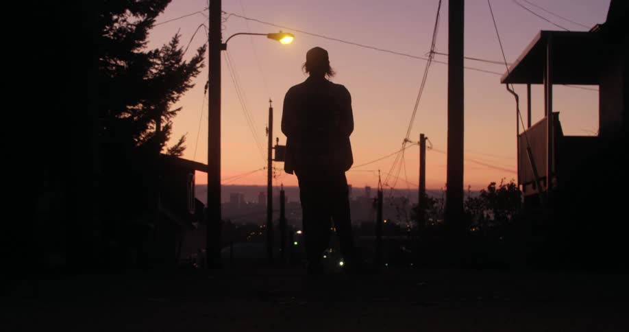 Mans silhouette rides on a skateboard in the neighborhood at dusk