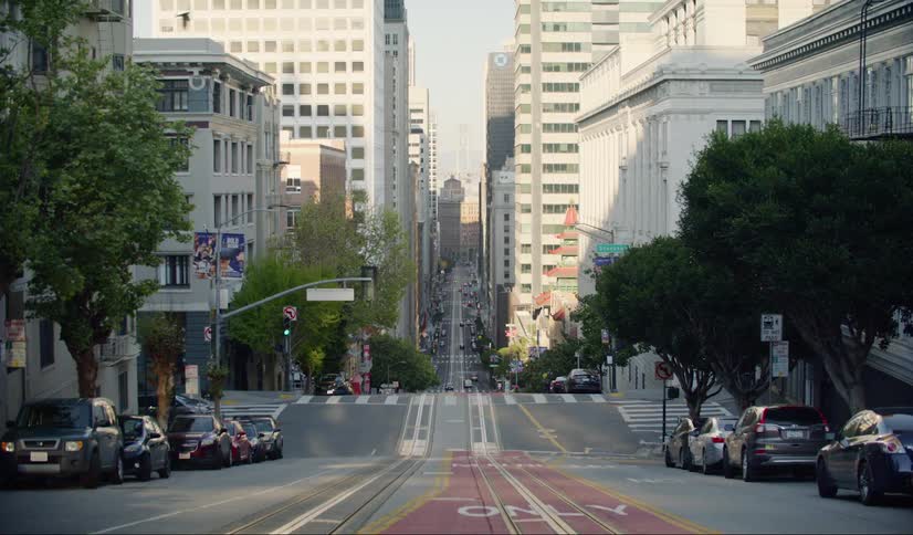 Cars parked on both sides of a hilly city street with trolley tracks down the center