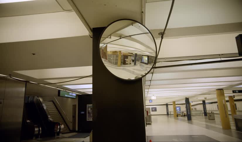 Mirror hangs on column near stairs and escalator reflecting empty room
