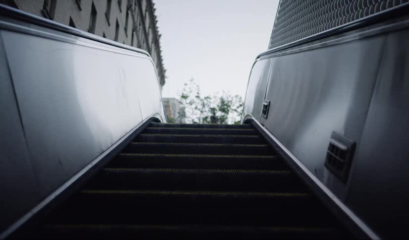 Camera rides up on an escalator leading to a city building