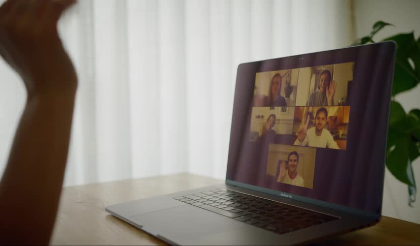 A person waves to others on the laptop display