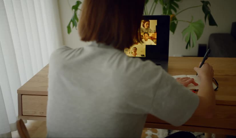 Woman sitting at the desk makes a video call and writes down in the living room at home