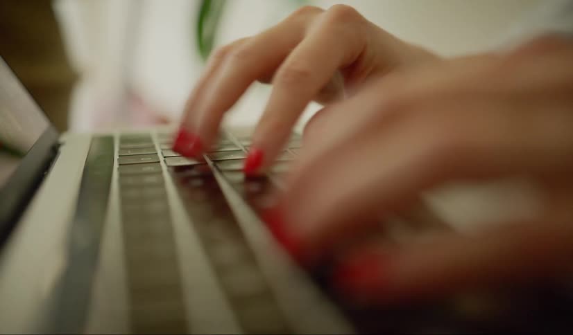 Woman with red nail polish types on laptop keyboard