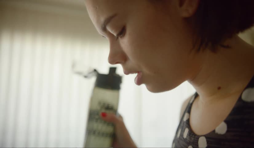 A woman stands in her flat drinking from a bottle