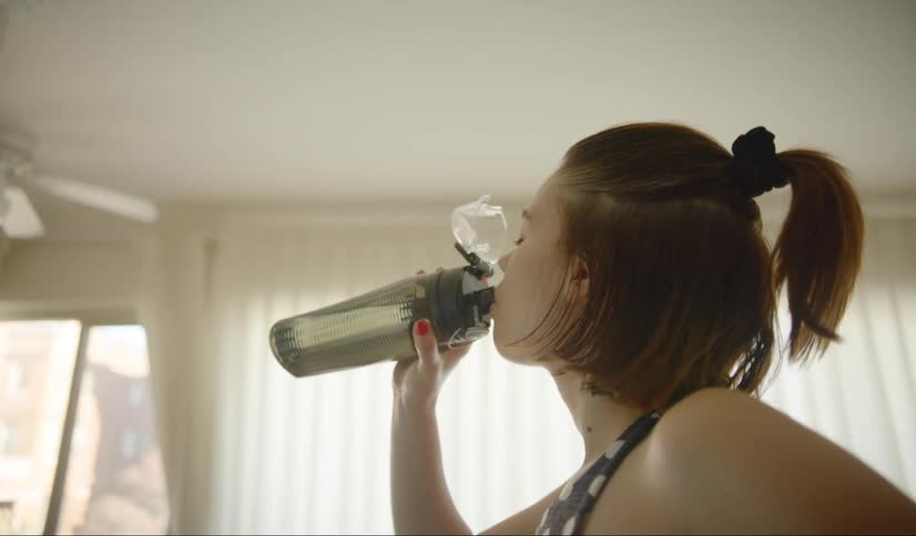 A teenager picks up her water bottle and takes a drink from it