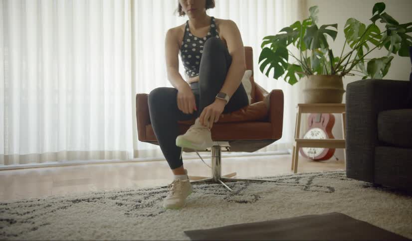 Woman puts on sneakers sitting in chair in living room