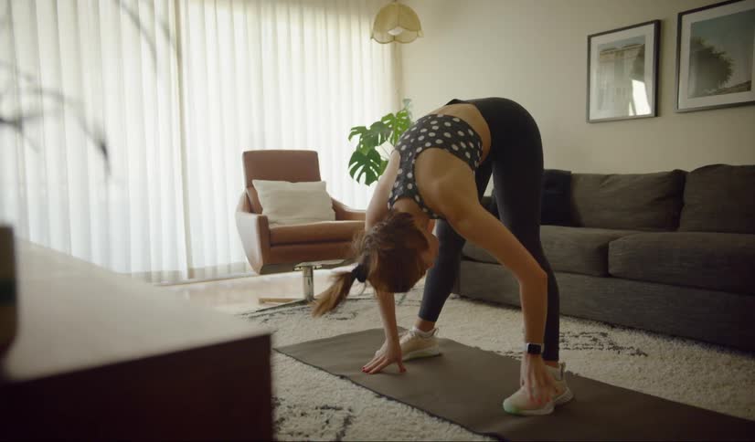 A woman stretches up and then down to her feet on a yoga mat