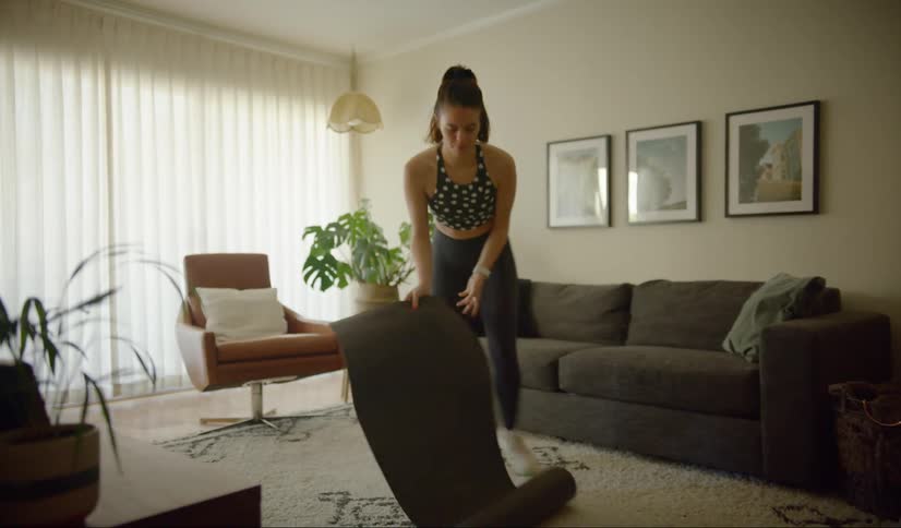 A woman spreading a yoga mat in a home living room