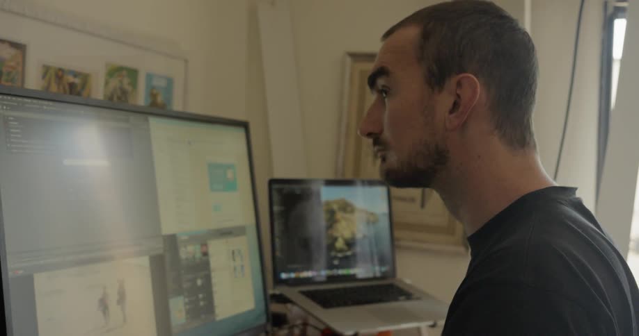 A man sitting before a monitor indoors during the day