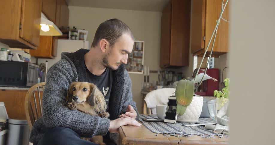 A man with a dog on his lap sits at a table and looks at his phone