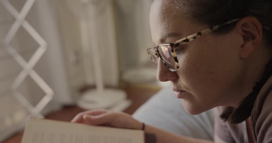 Woman lying down on the bed reads a book in the bedroom