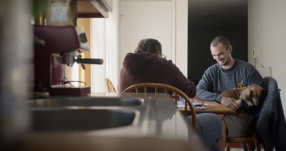 Male holding pet dog while playing card game with friends indoors