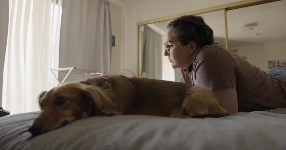 A woman lays on her bed beside a dog
