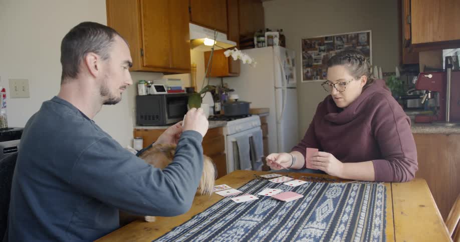 Couple with dog sitting on table playing cards in an apartment