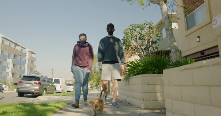 Man and woman wearing face masks walk a sausage dog on the pavement