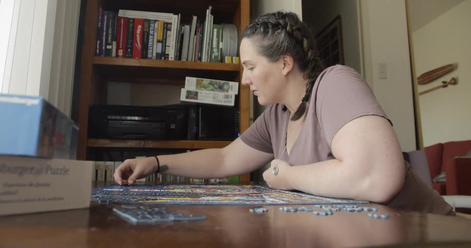 Female sitting at a table concentrating while putting together a puzzle by herself