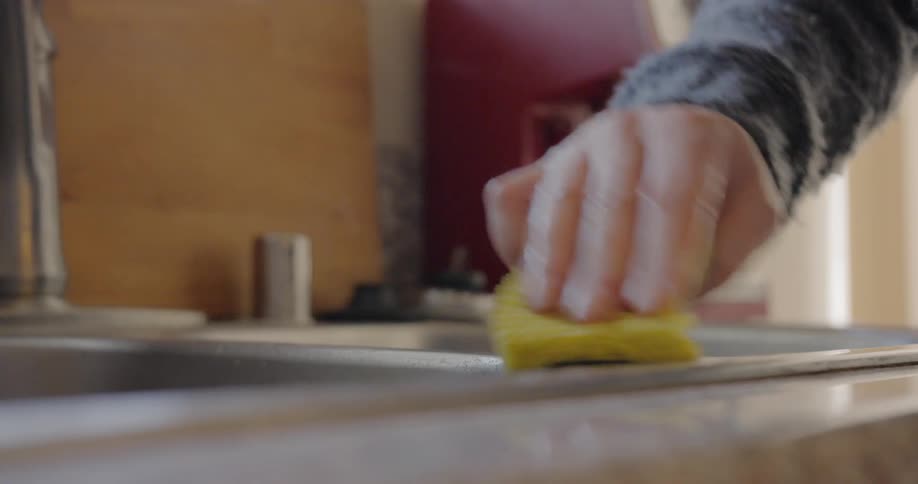 Close up of mans hand wiping kitchen sink with a sponge