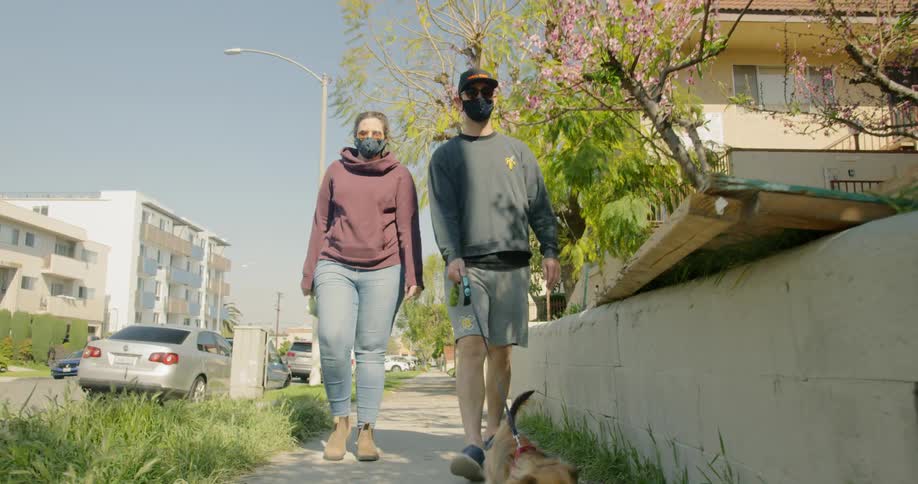 Man and woman wearing face masks walk the tiny dog on the pavement