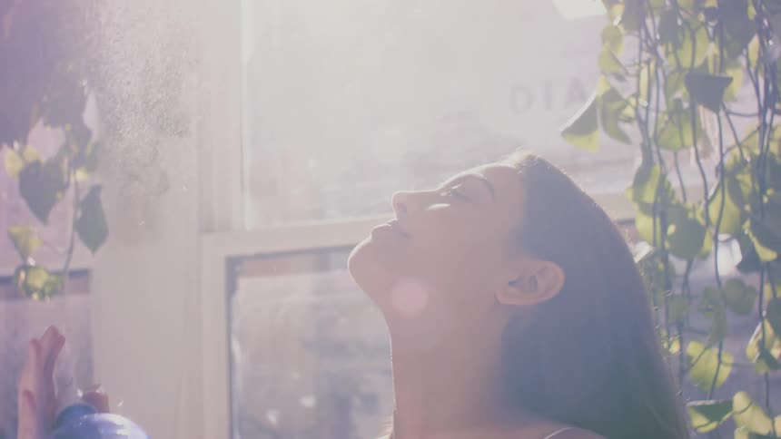 A woman sprays a mist of water above her and puts her face in to it