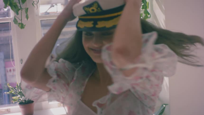 A woman spins and dances around in her apartment filled with houseplants