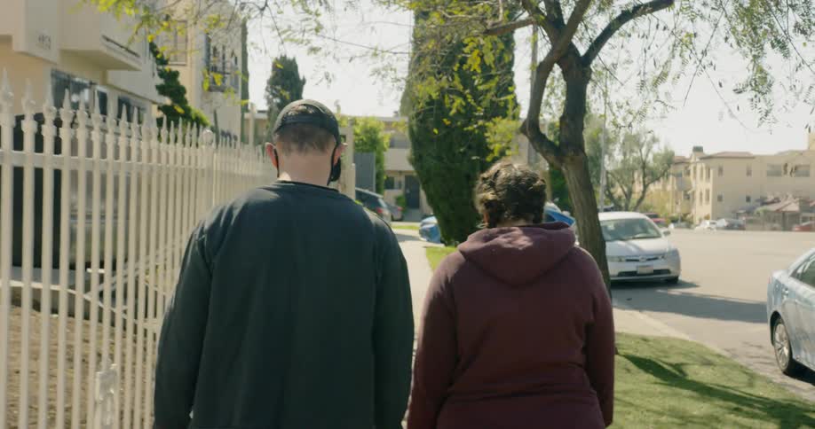 A couple walks down the sidewalk in a suburban area wearing face masks