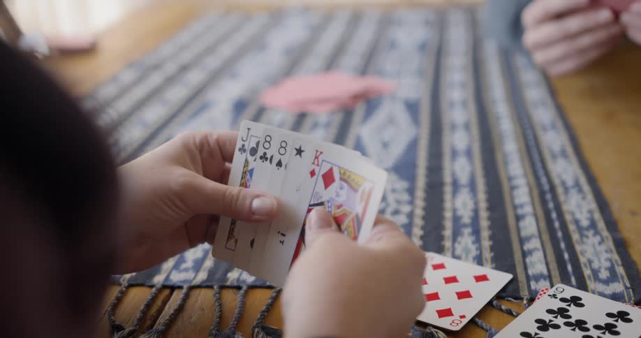 A woman holds playing cards in her hands while sitting at the table across from the person she is playing with