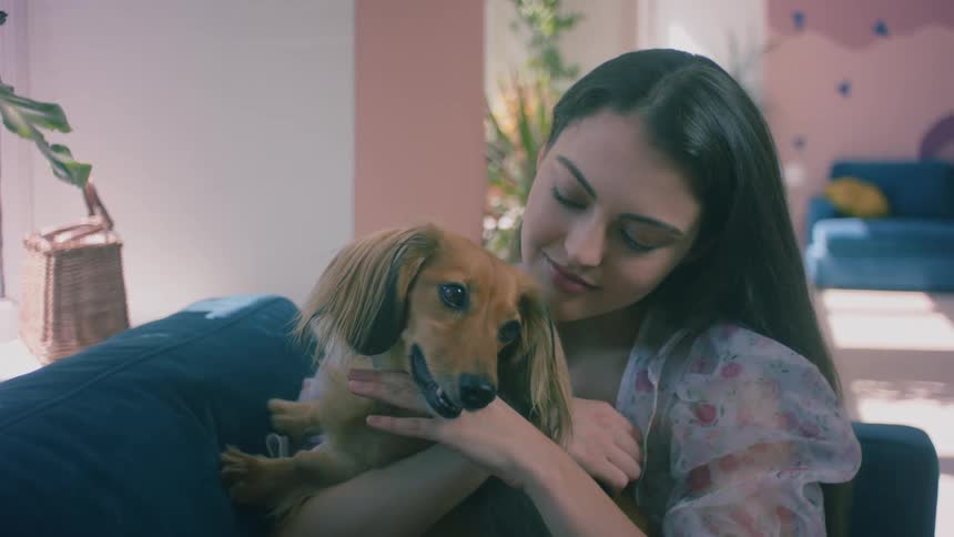 A woman sitting indoors on a sofa hugging a small dog