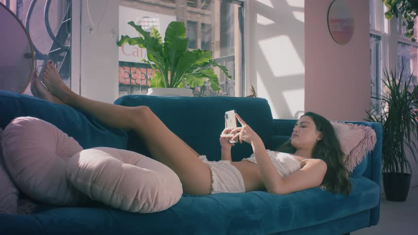 A teenager lies on a couch and looks at her cell phone