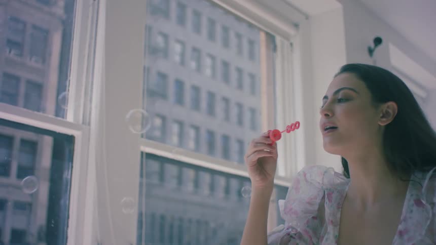 A young woman blows bubbles near a window
