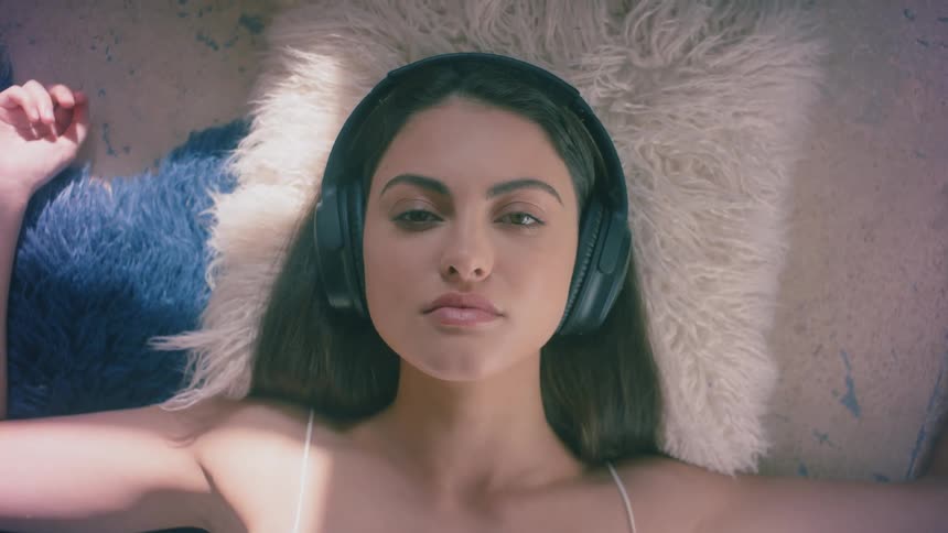 Woman wearing headphones while laying on pillows open her eyes