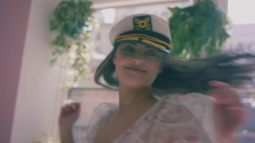 A woman wearing a dress and military style cap dances in a room