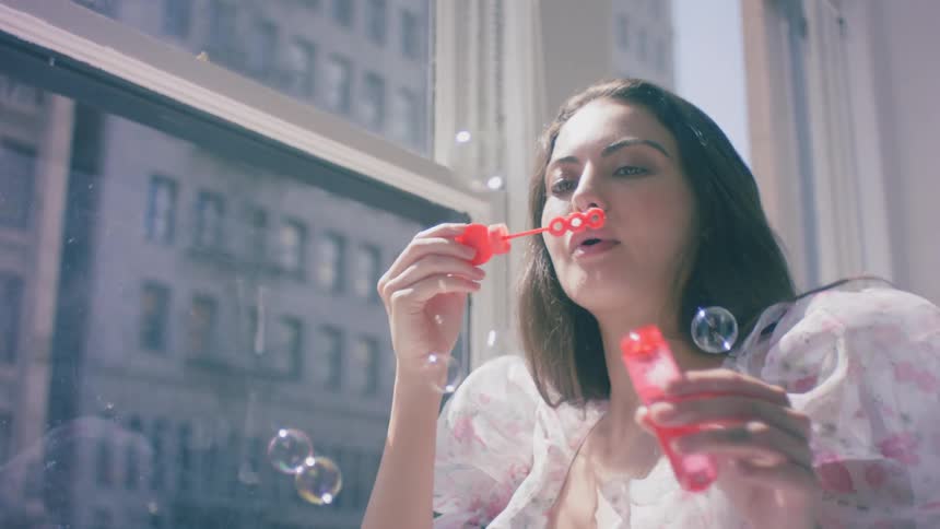 Brunette woman blows soap bubbles at home during daylight