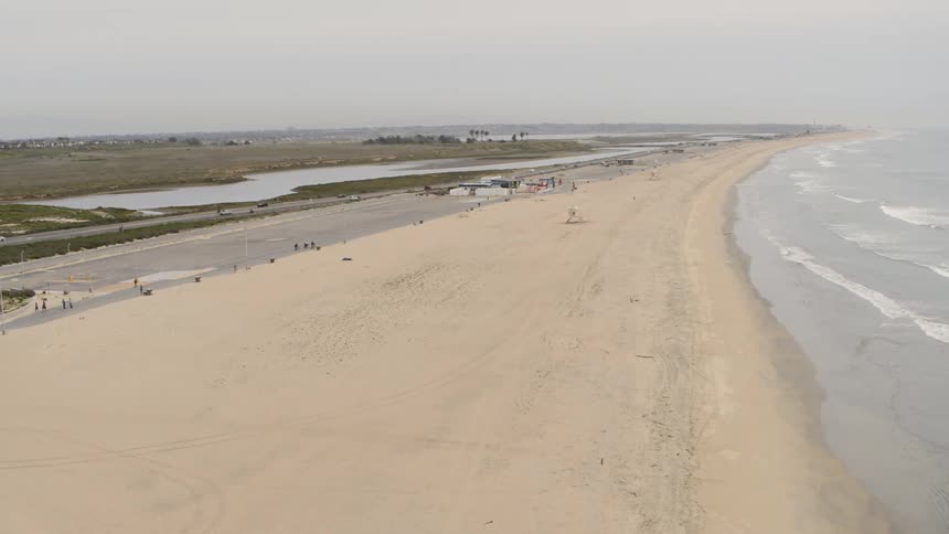 A beach coast with a road near it with beachgoers and cars going back and forth
