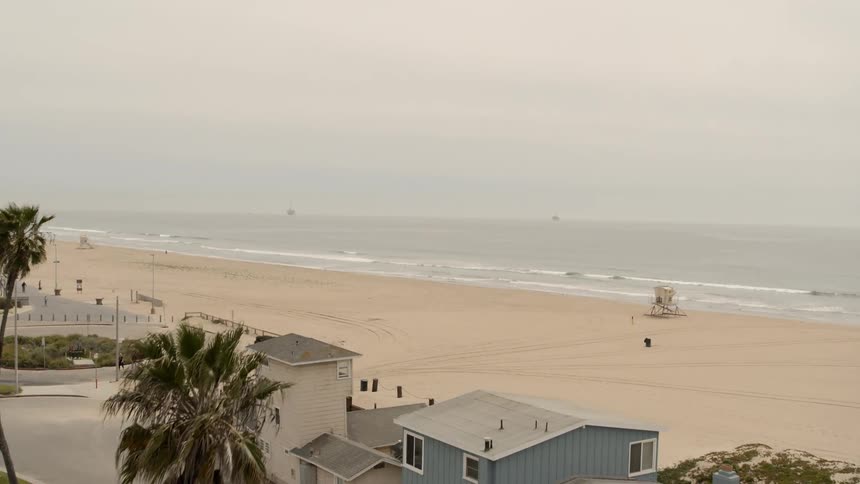 A car travels past home on the coast with empty sandy beach behind and only a few people walking on the path