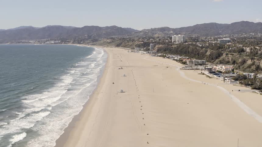 Wide beach separates ocean from buildings of sprawling city bordered by mountains