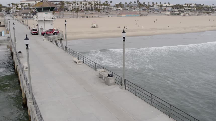 A pier goes into the ocean over a beach with spread out patrons
