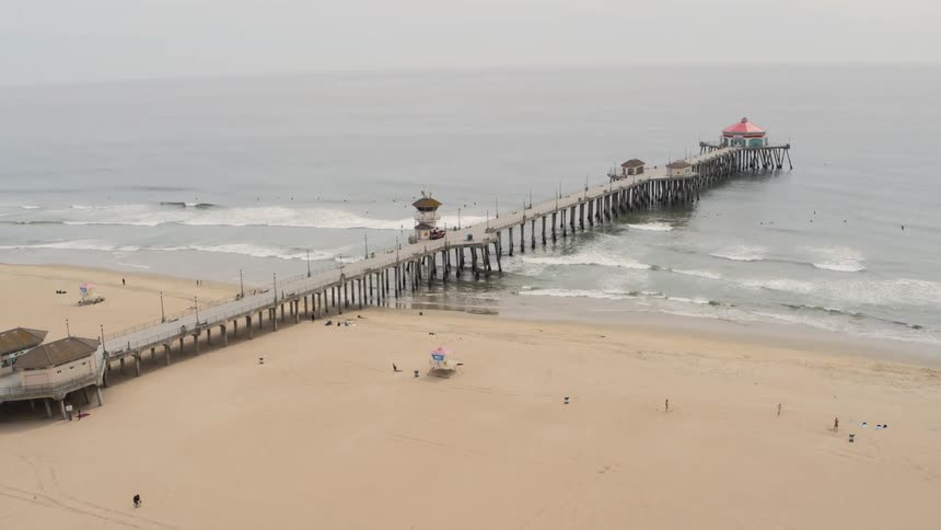 A pier juts out into the ocean on a sparsely populated beach