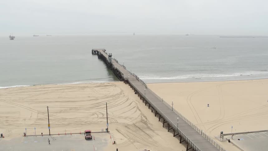 A pier extends into a coast beach with boats in the background