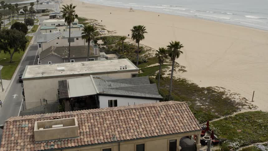 Ocean waves come to shore on an empty beach with homes and apartment buildings along the shore