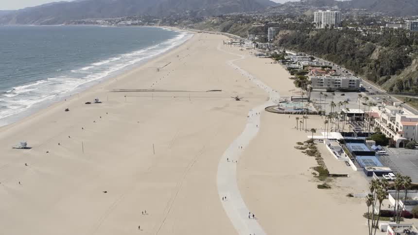 Aerial view of the sandy beach next to the ocean and people walking on the road on a sunny day