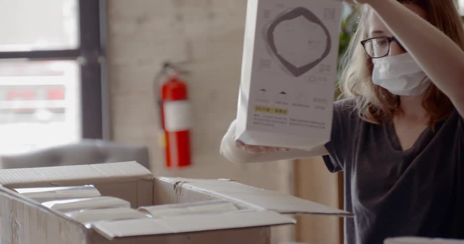 A woman wearing a medical mask pulls a product out of a shipping box