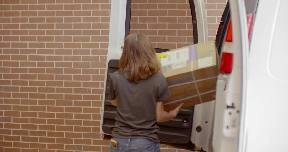 Woman wearing face mask unloads cardboard boxes from a van to a lift