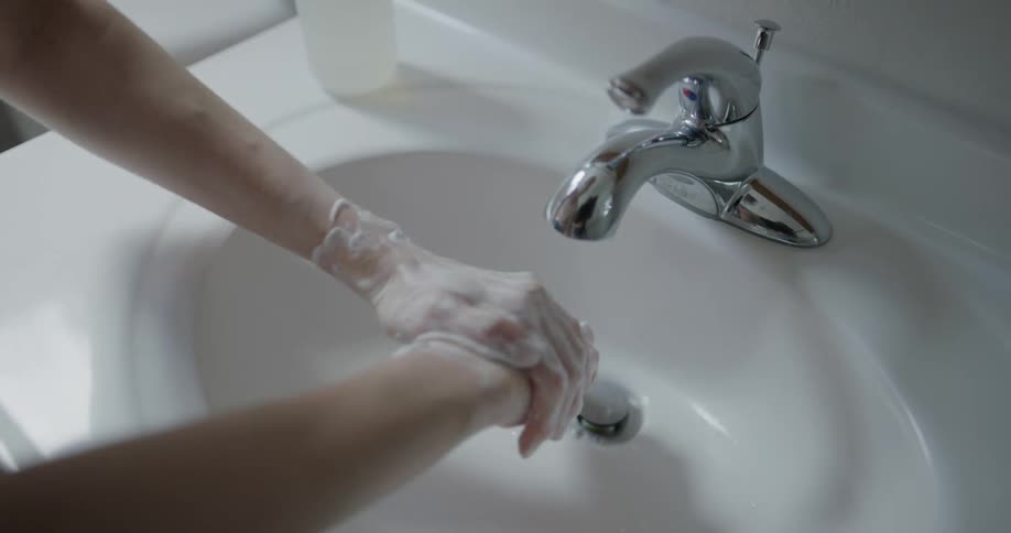 A woman thoroughly washes her hands with soap at the bathroom sink without the water running