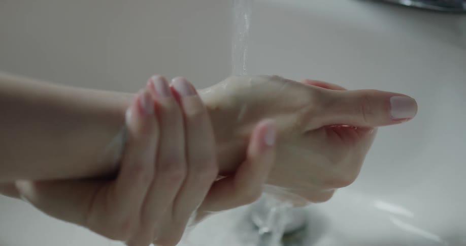 A person washing their soapy hands under a faucet
