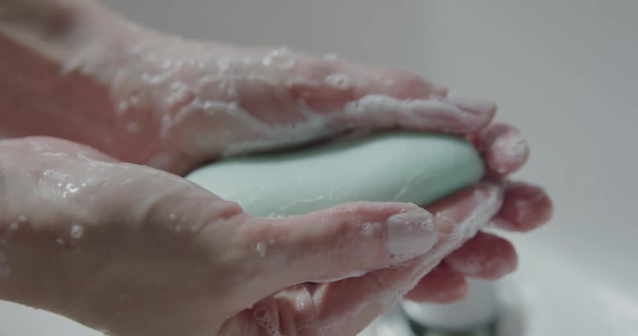 Person washes hands with soap on bathroom sink