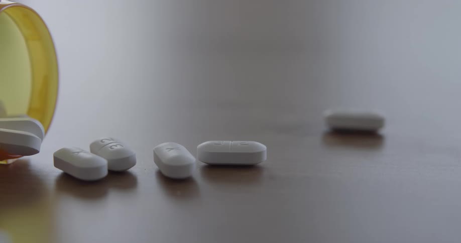 Pill bottle falls onto its side spilling tablet onto the table
