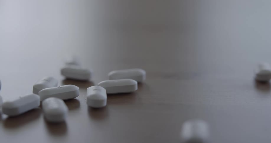 White capsules with the letter x on them are spilled onto a table