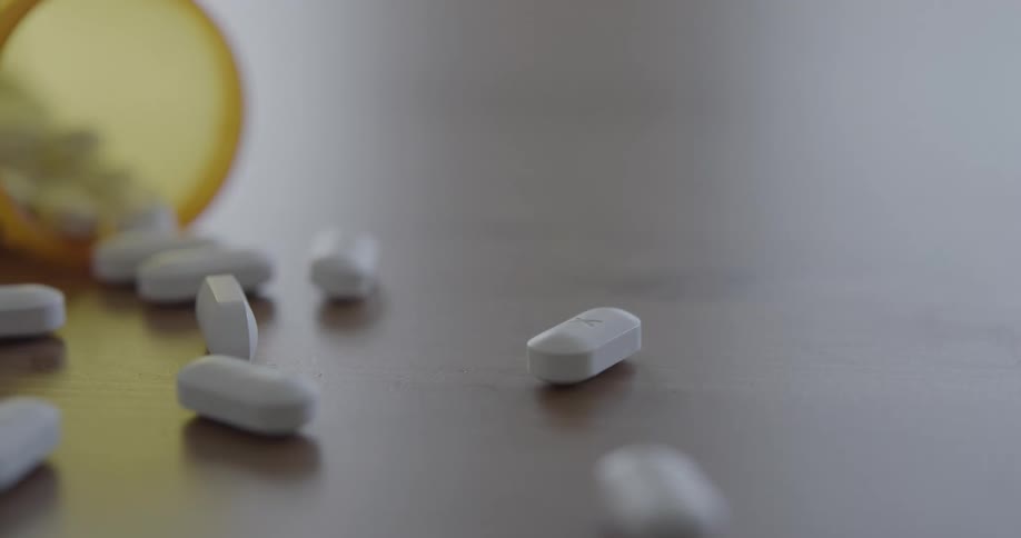 White pills spilling onto a wooden table out of a container