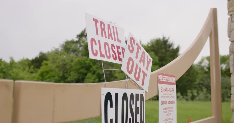 A fence with signs with grass and trees in the background