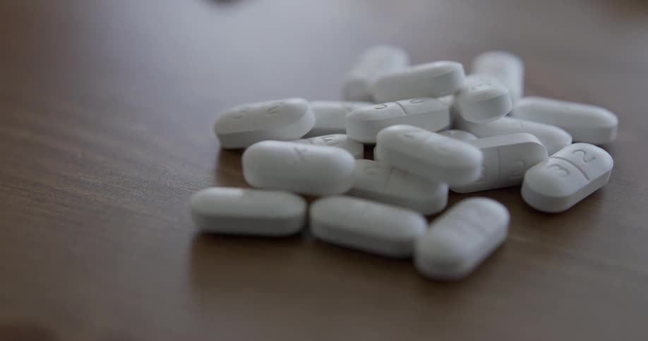 A hands pours pills onto a wooden table